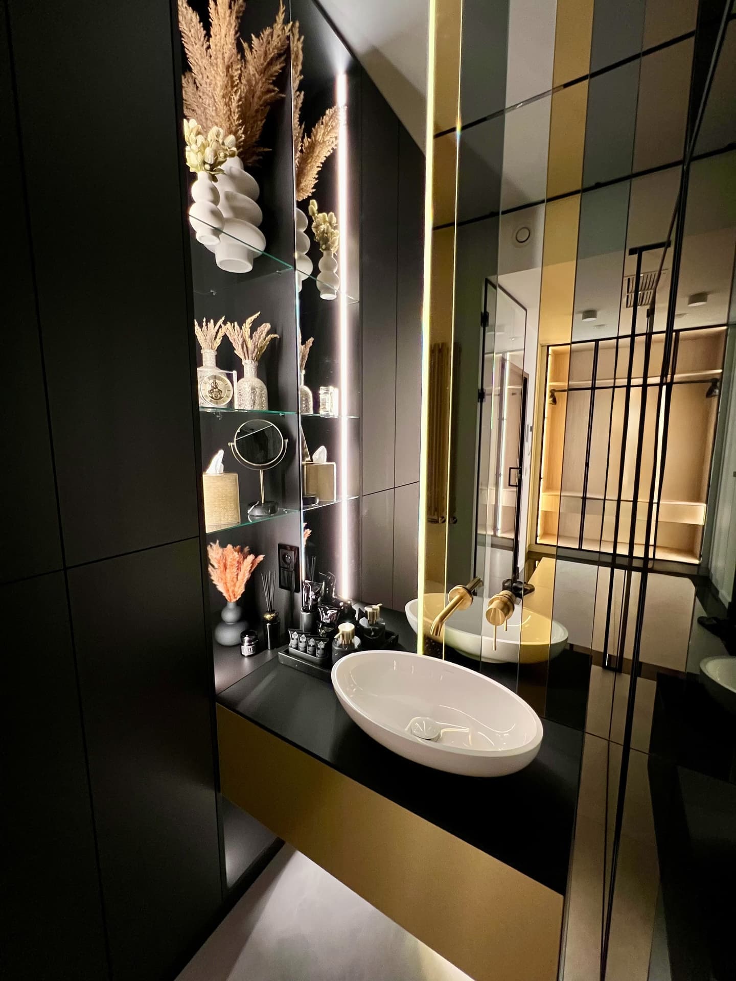 Designer bathroom with oval basin, glass shelves with pampas grass and gold faucet