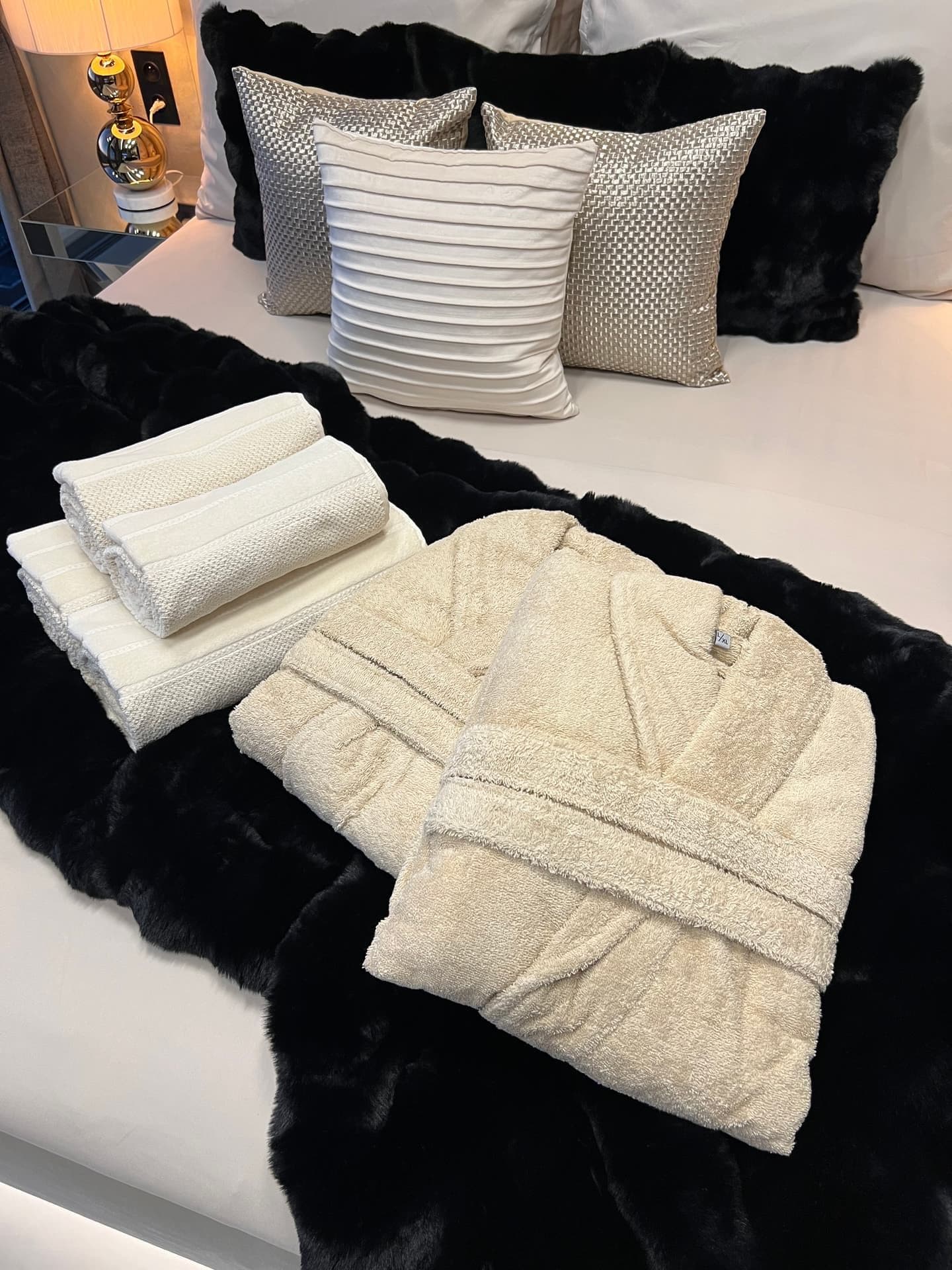 Bathrobe and folded towels laid out on bed with decorative cushions
