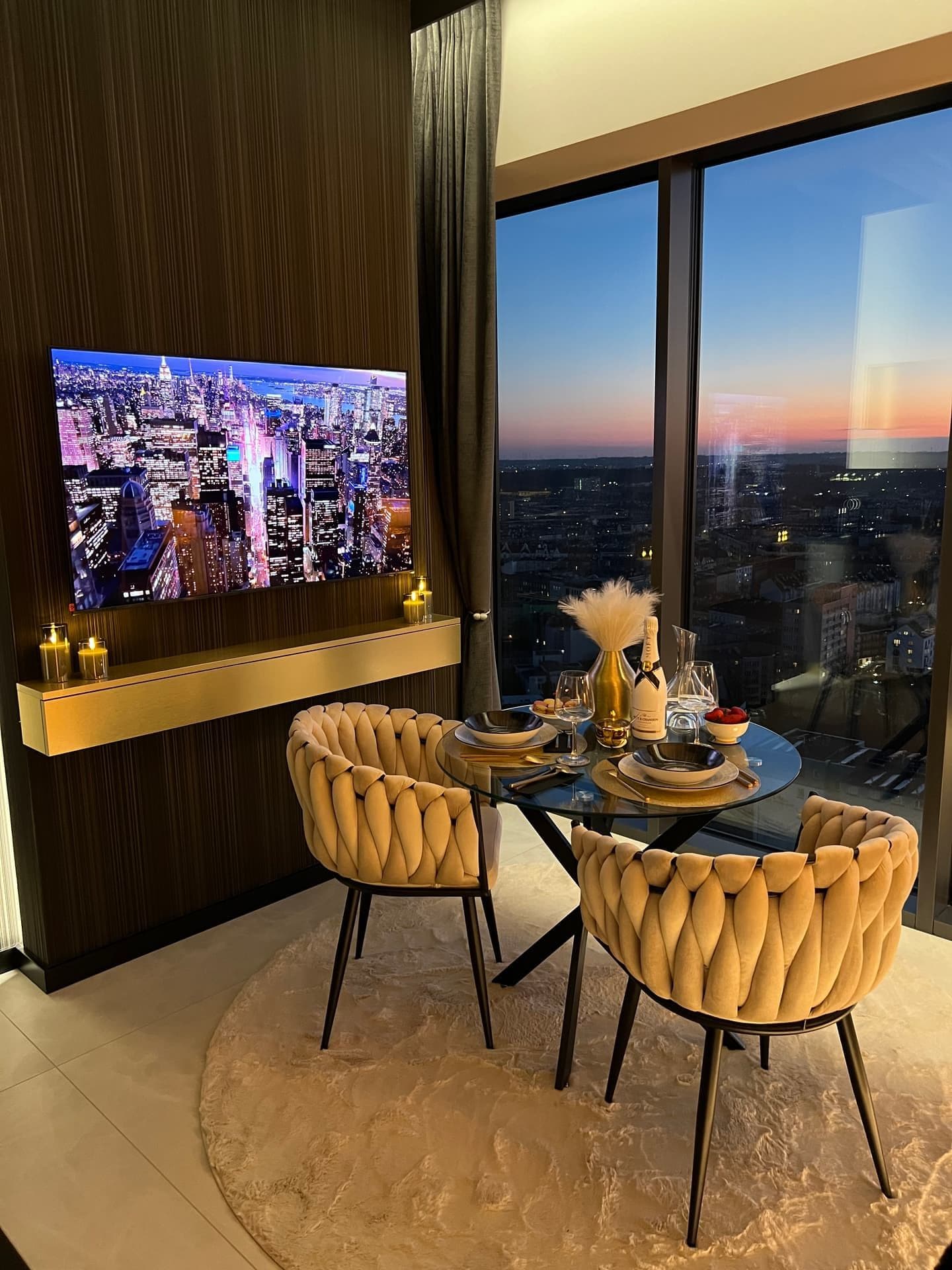 Dining corner with TV on, set table and panoramic twilight view