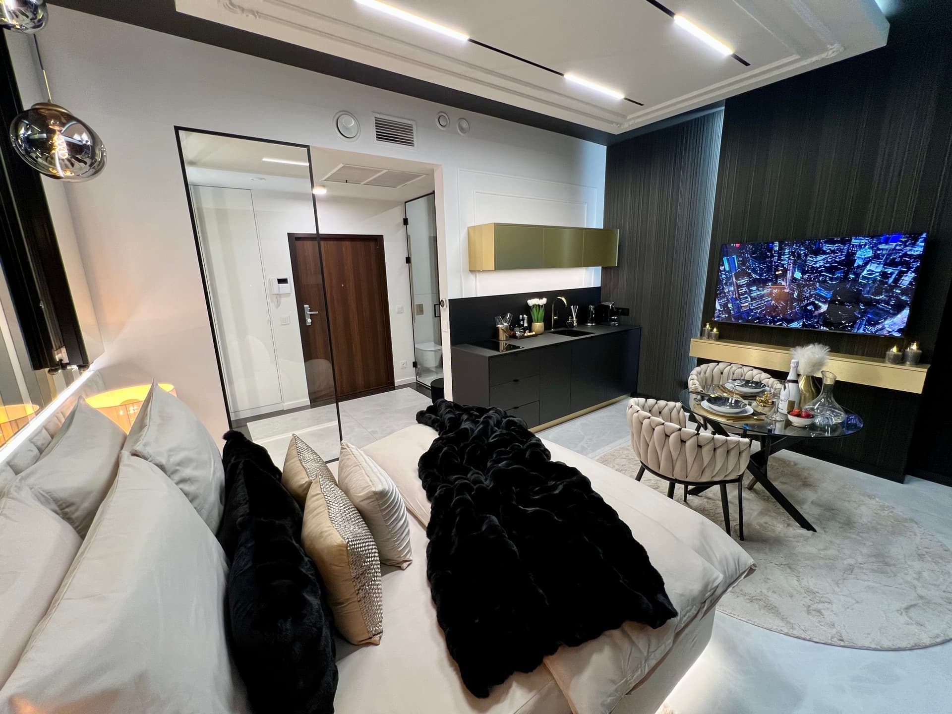 Interior night view: bed with throw, entry door, TV and kitchenette