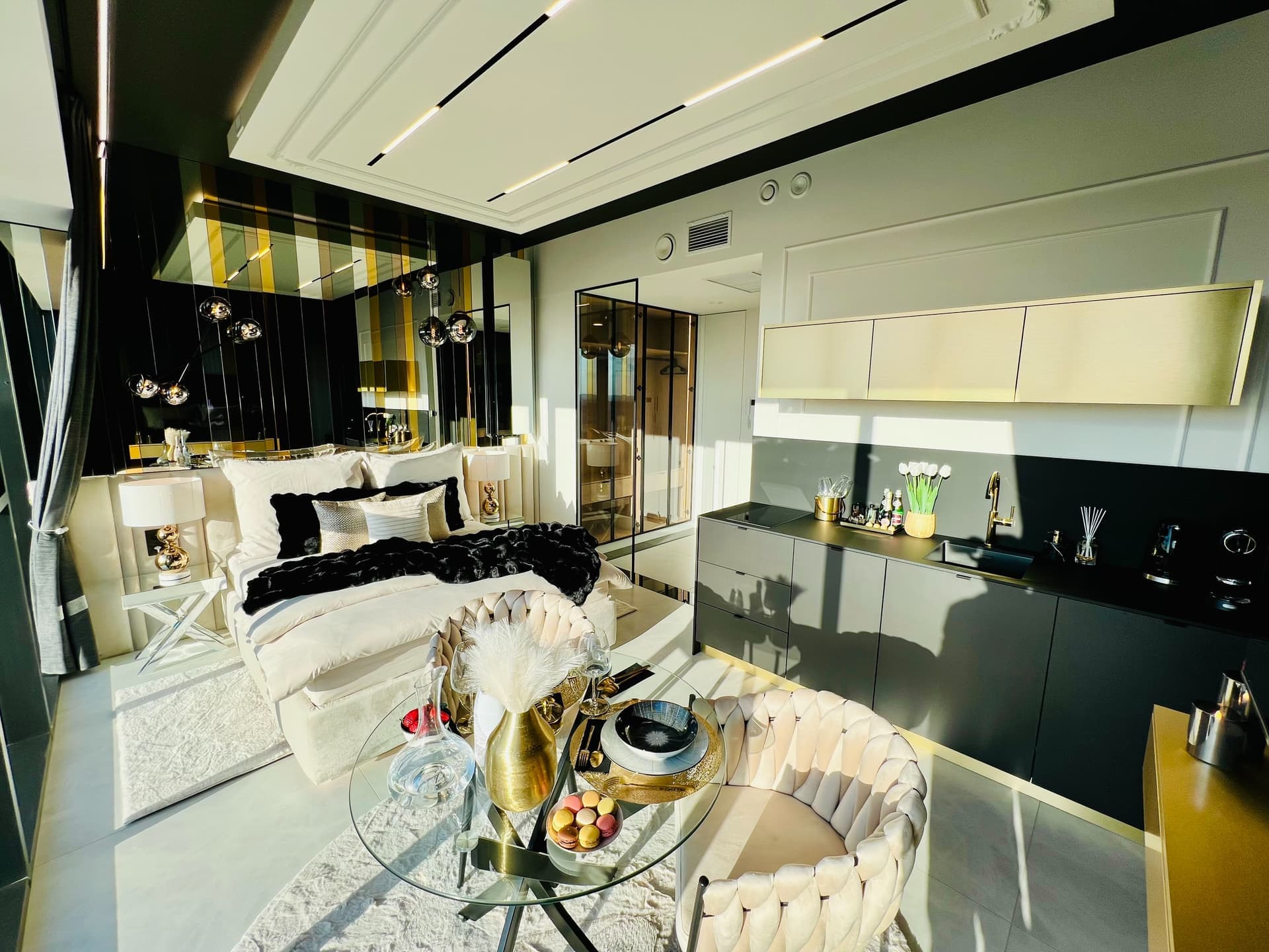 Suite in daylight: bed, table with macarons, kitchenette and glass bathroom