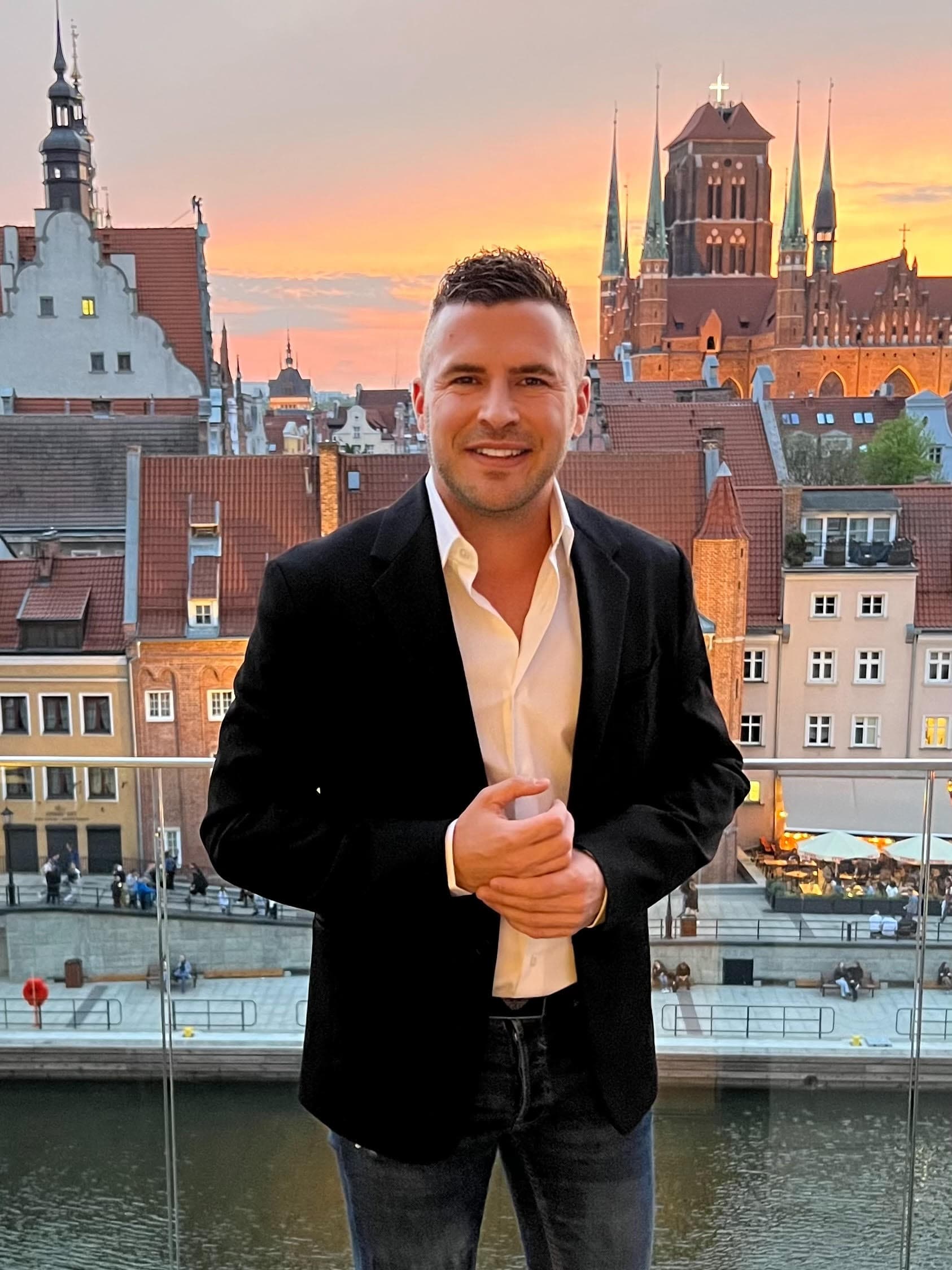 Jean Huillet in blazer with Gdansk old town at sunset in background
